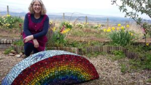 Local mosaic artist JudyJamJar with her latest creation, a giant rainbow inspired by the rainbow paintings made by the children in the village of Kippen. It sits in her front garden to be enjoyed by anyone walking past.